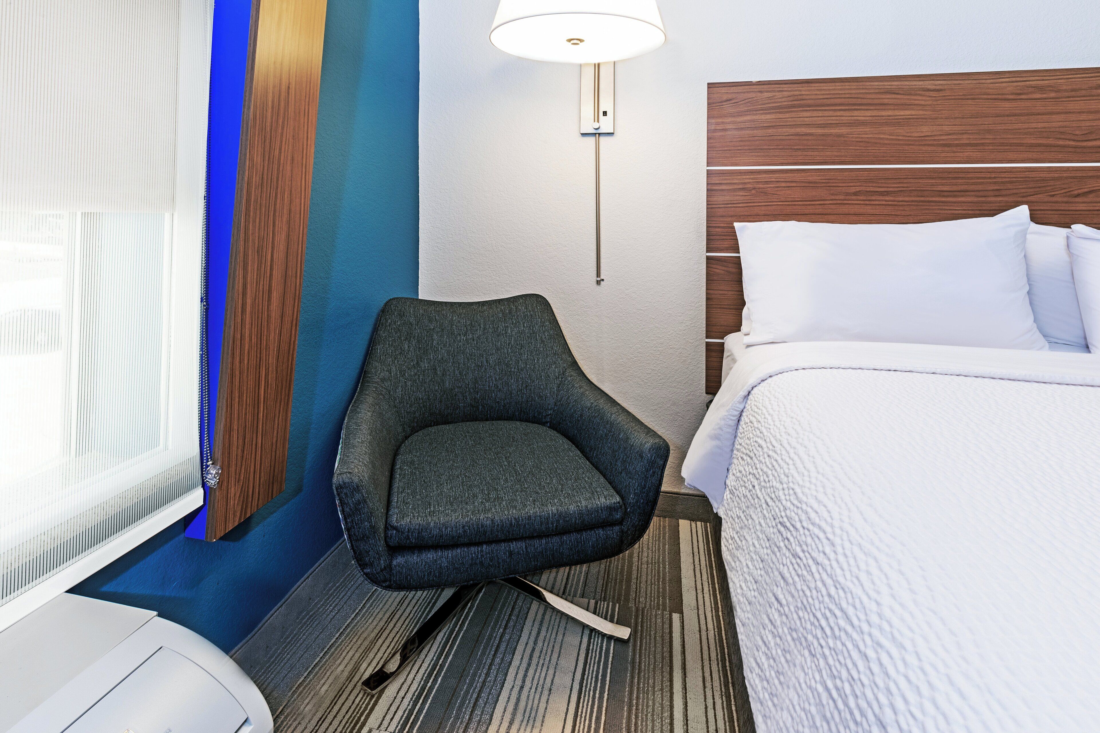 Ein Hotelzimmer mit einem Bett, einem Sessel, einer Lampe und einem Fenster mit Jalousien.