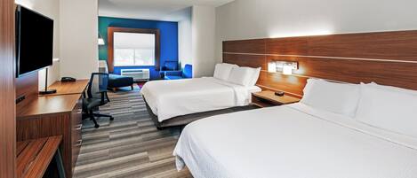 Ein Hotelzimmer mit zwei Betten, einem Schreibtisch, einem Fernseher und einer Sitzecke mit Sessel und Tisch.