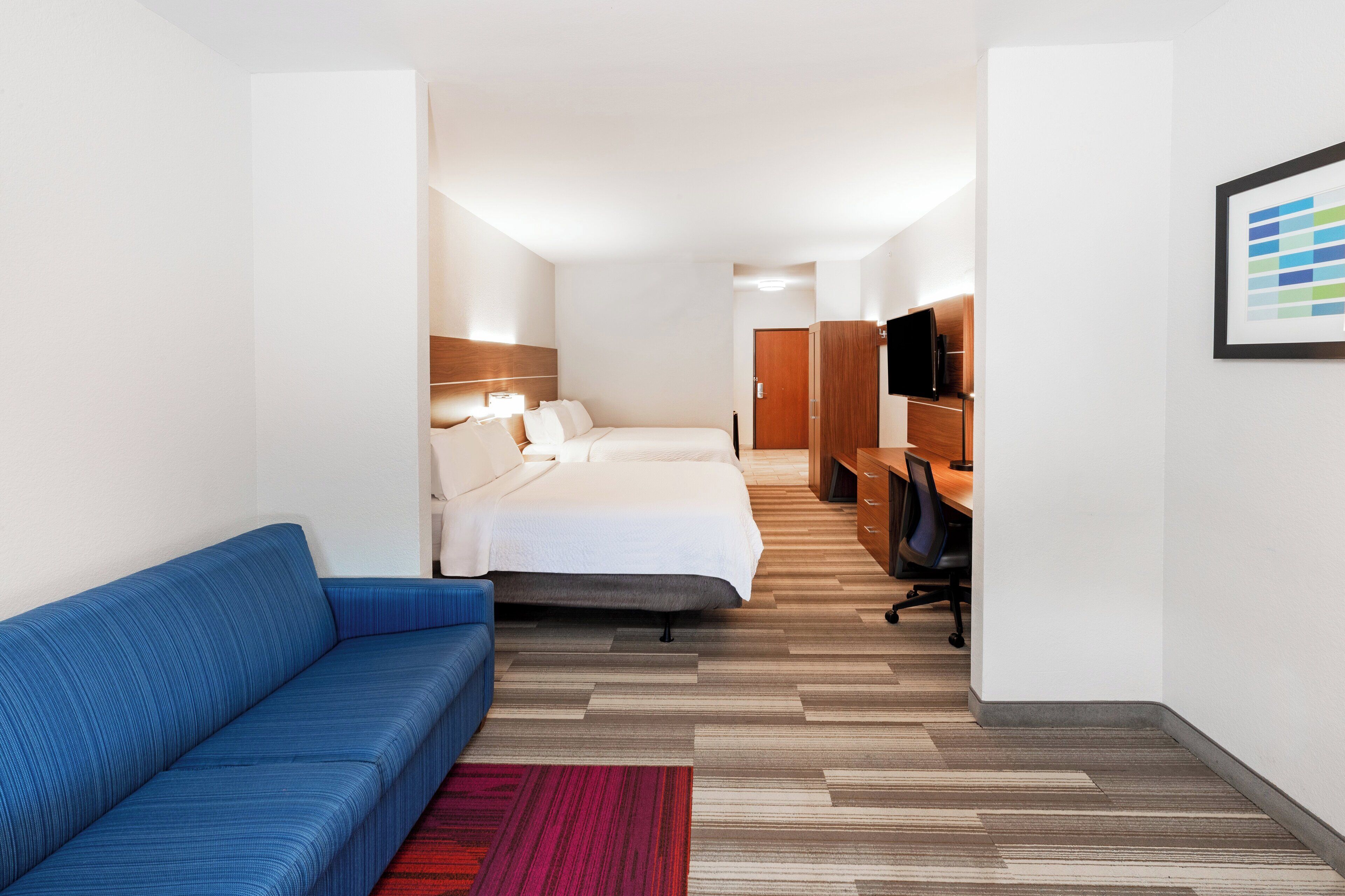 Een hotelkamer met een bed, een blauwe bank, een bureau met een stoel, een televisie en een ingelijst kunstwerk aan de muur.