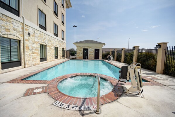 A swimming pool with a hot tub, surrounded by a brick deck and a stone building.