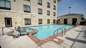 A swimming pool with a hot tub, stone walls, and a small building with a door.