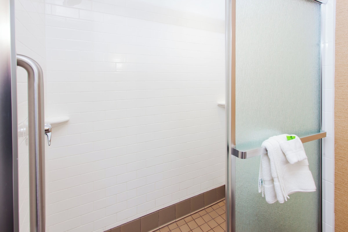 A bathroom with white tiled walls, a glass shower enclosure, and a towel rack with folded towels.