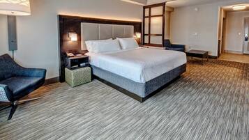 A hotel room with a large bed, a desk, a chair, and a bedside table.