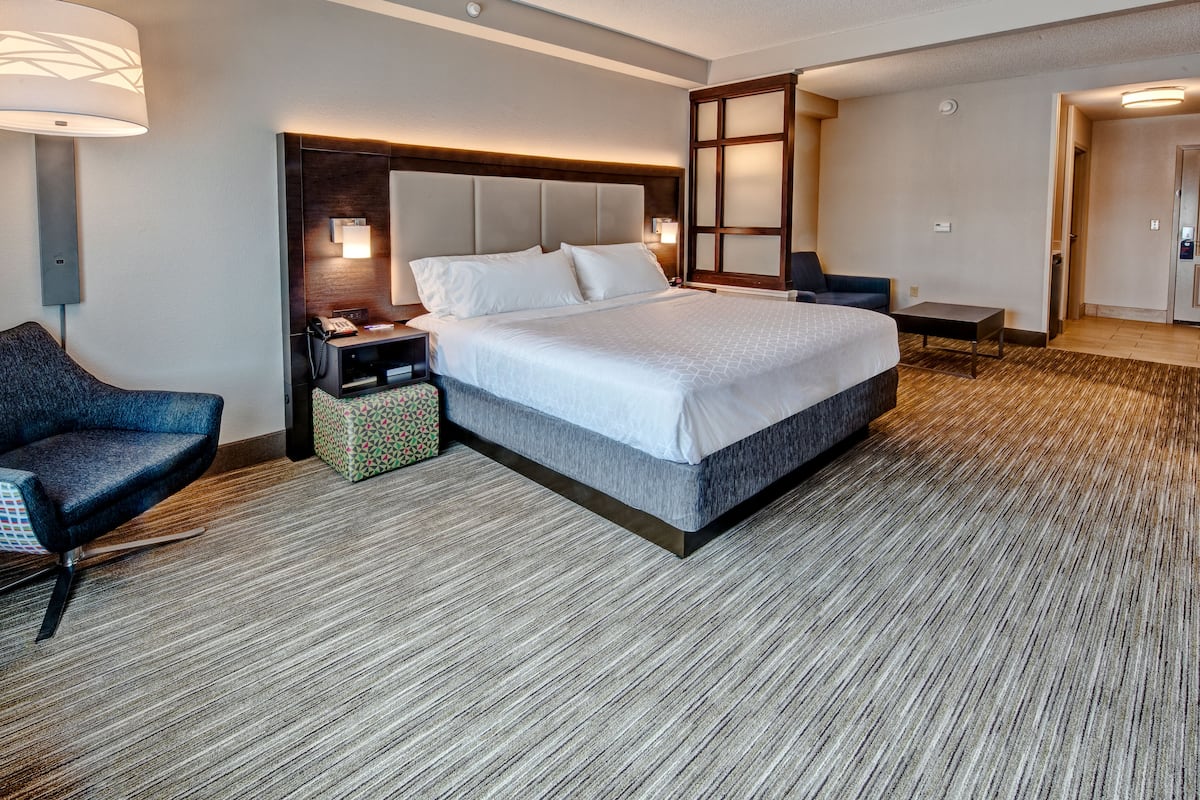 Une chambre d’hôtel moderne, dotée d’un grand lit, d’un bureau, d’une chaise et d’une table de chevet avec une lampe.