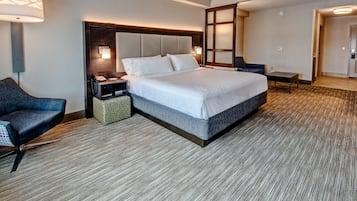 Ein modernes Hotelzimmer mit einem großen Bett, einem Schreibtisch, einem Stuhl und einem Nachttisch mit Lampe.