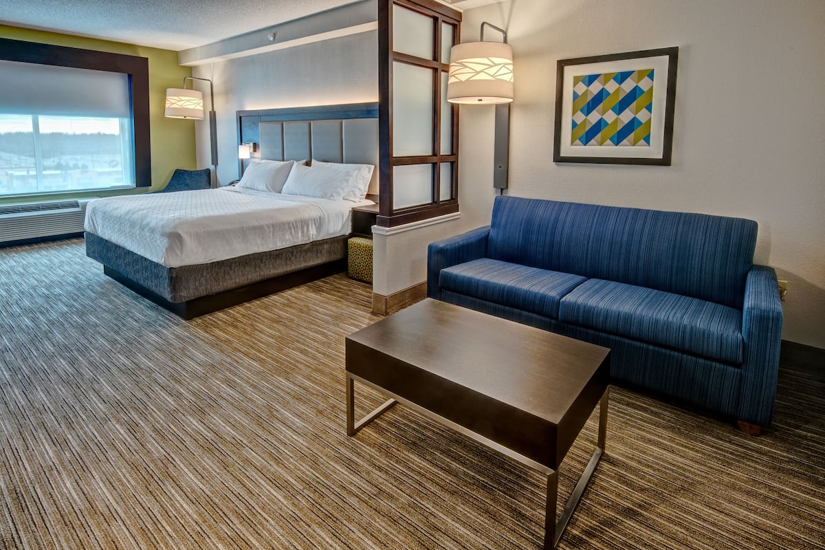 Une chambre d’hôtel avec un lit, un canapé bleu, une table basse et une grande fenêtre.