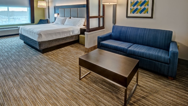 A hotel room with a bed, a blue sofa, a coffee table, and a large window.