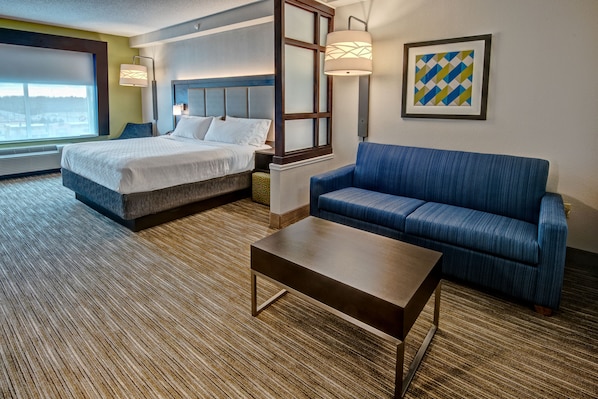 A hotel room with a bed, a blue sofa, a coffee table, and a large window.