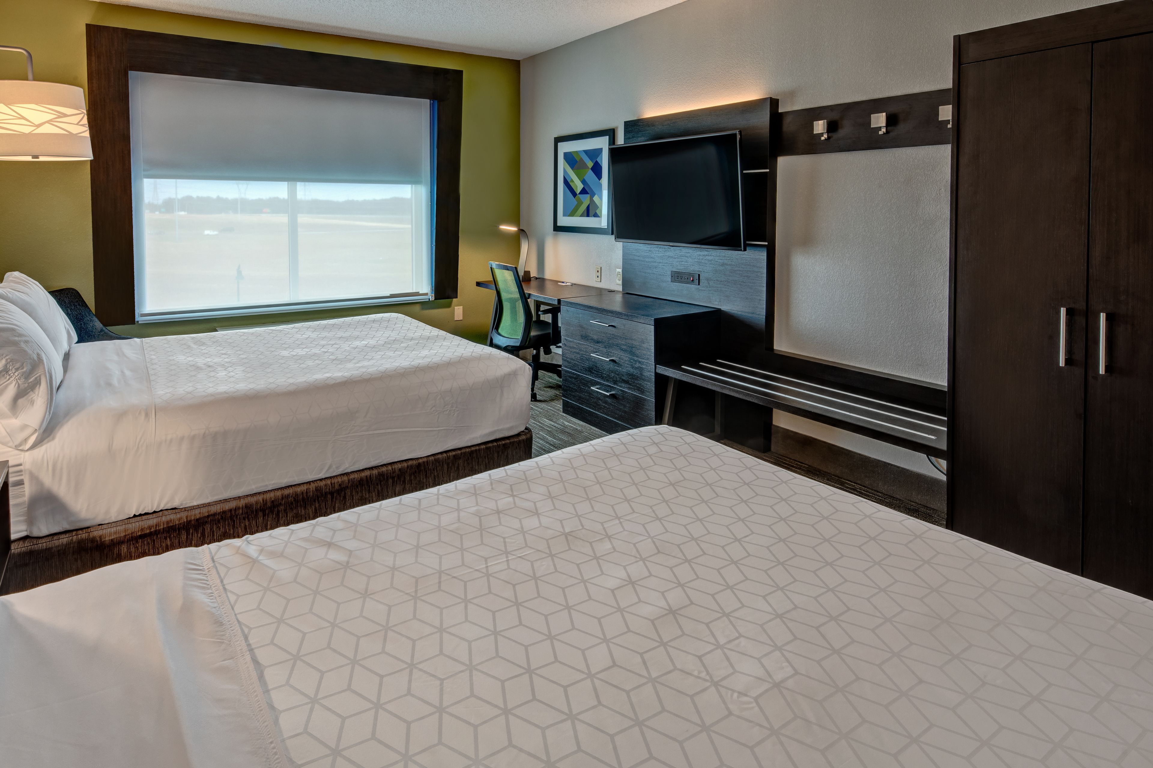 Una habitación de hotel con dos camas, un escritorio, una silla, un televisor y un armario.