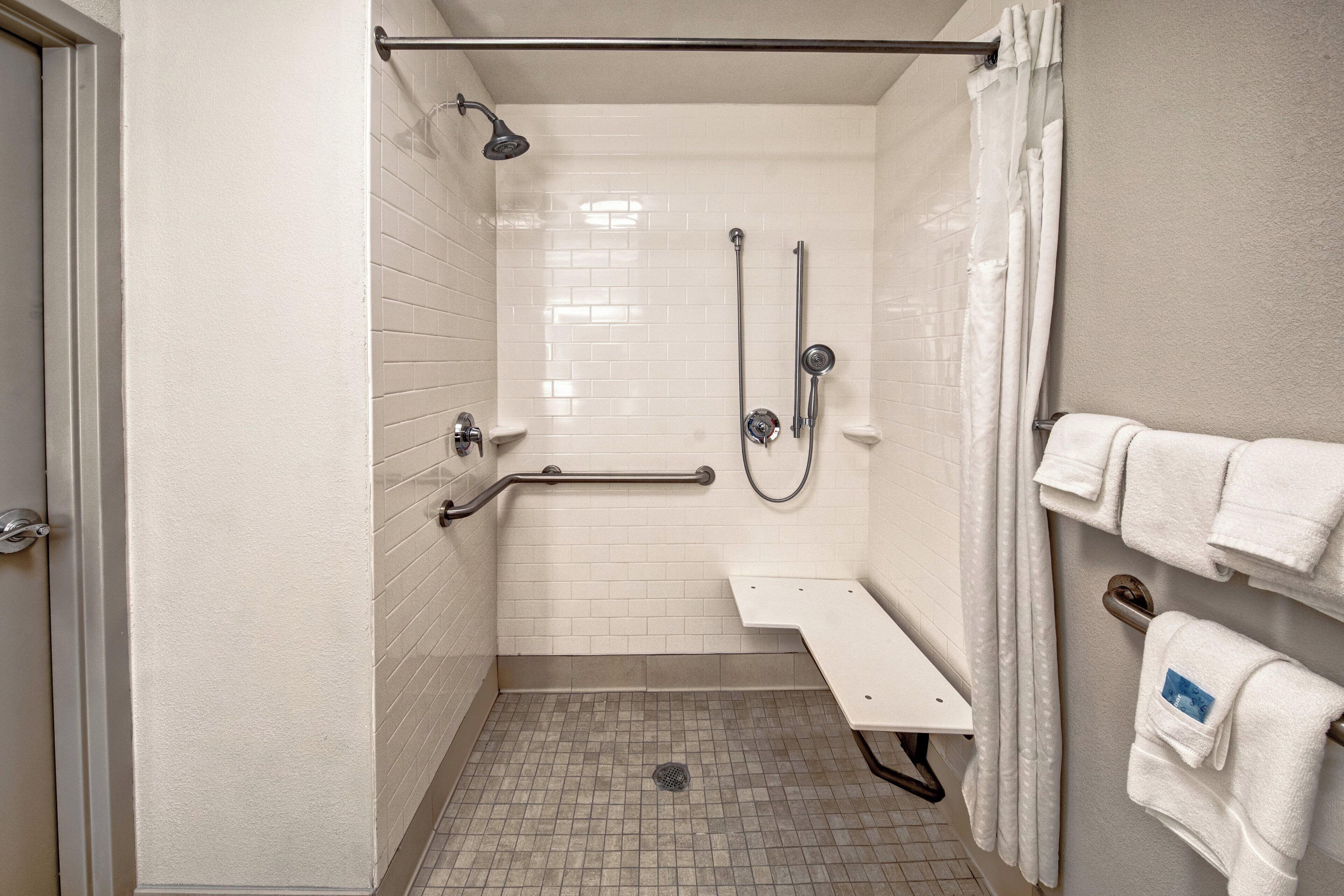 A shower area with a grab bar, a handheld showerhead, a wall-mounted faucet, and a towel rack with towels.