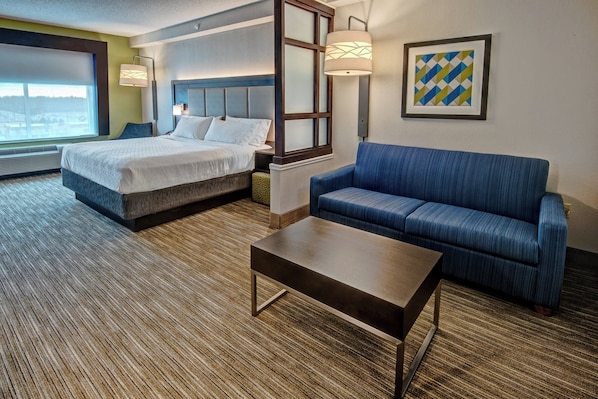A hotel room with a bed, a sofa, a coffee table, and a large window.