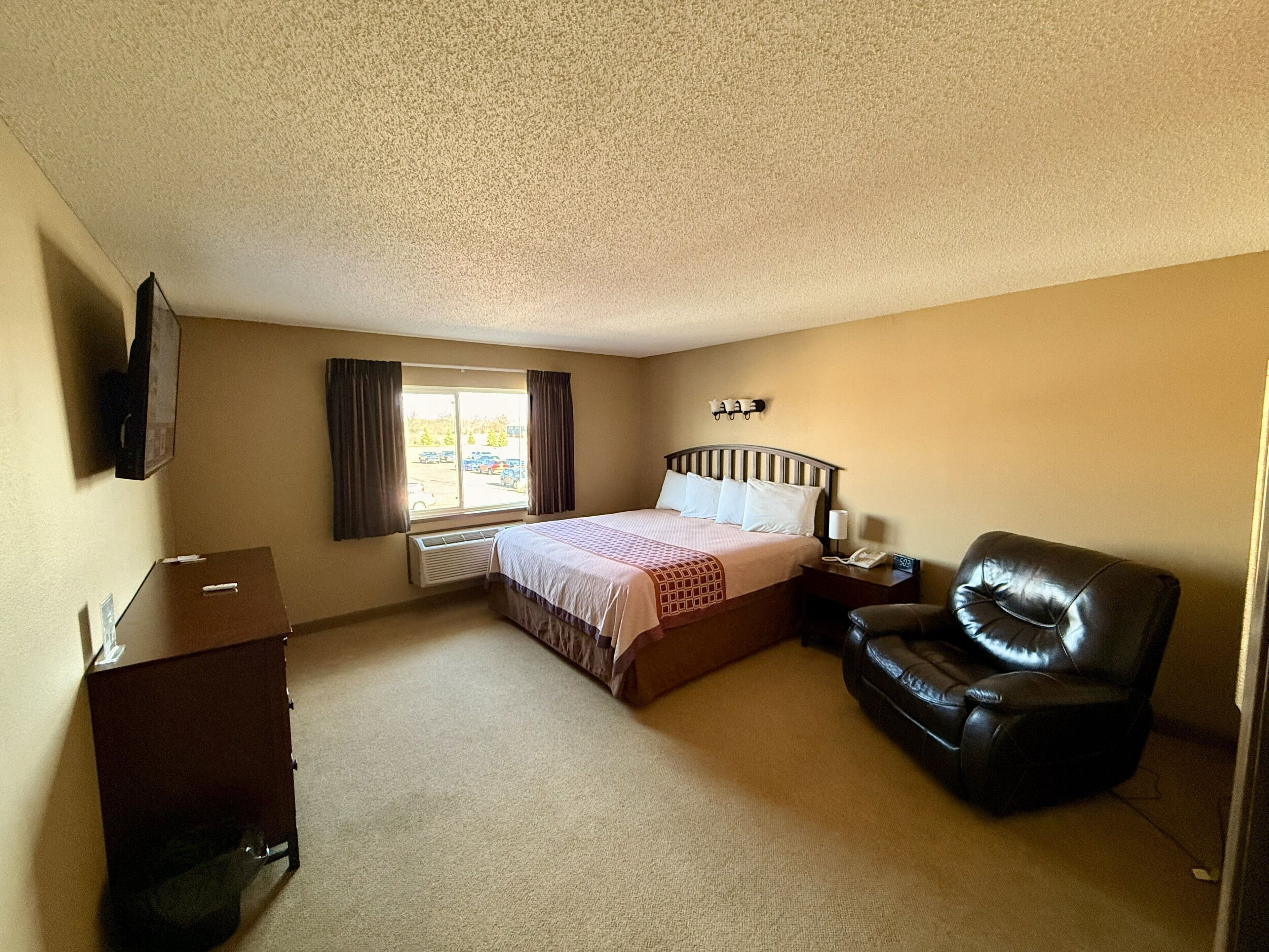 Ein Hotelzimmer mit Bett, Schreibtisch, Stuhl, Fernseher und einem fensterbepflanzten Fenster.