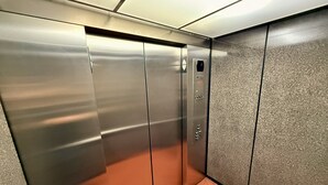 Een lift met metalen deuren, een bedieningspaneel en een gestructureerde wand.
