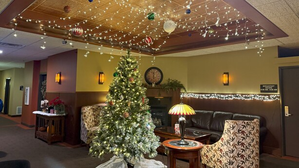 Een ontvangsthal met een kerstboom, een klok, een open haard en een bord met de ontbijttijden.