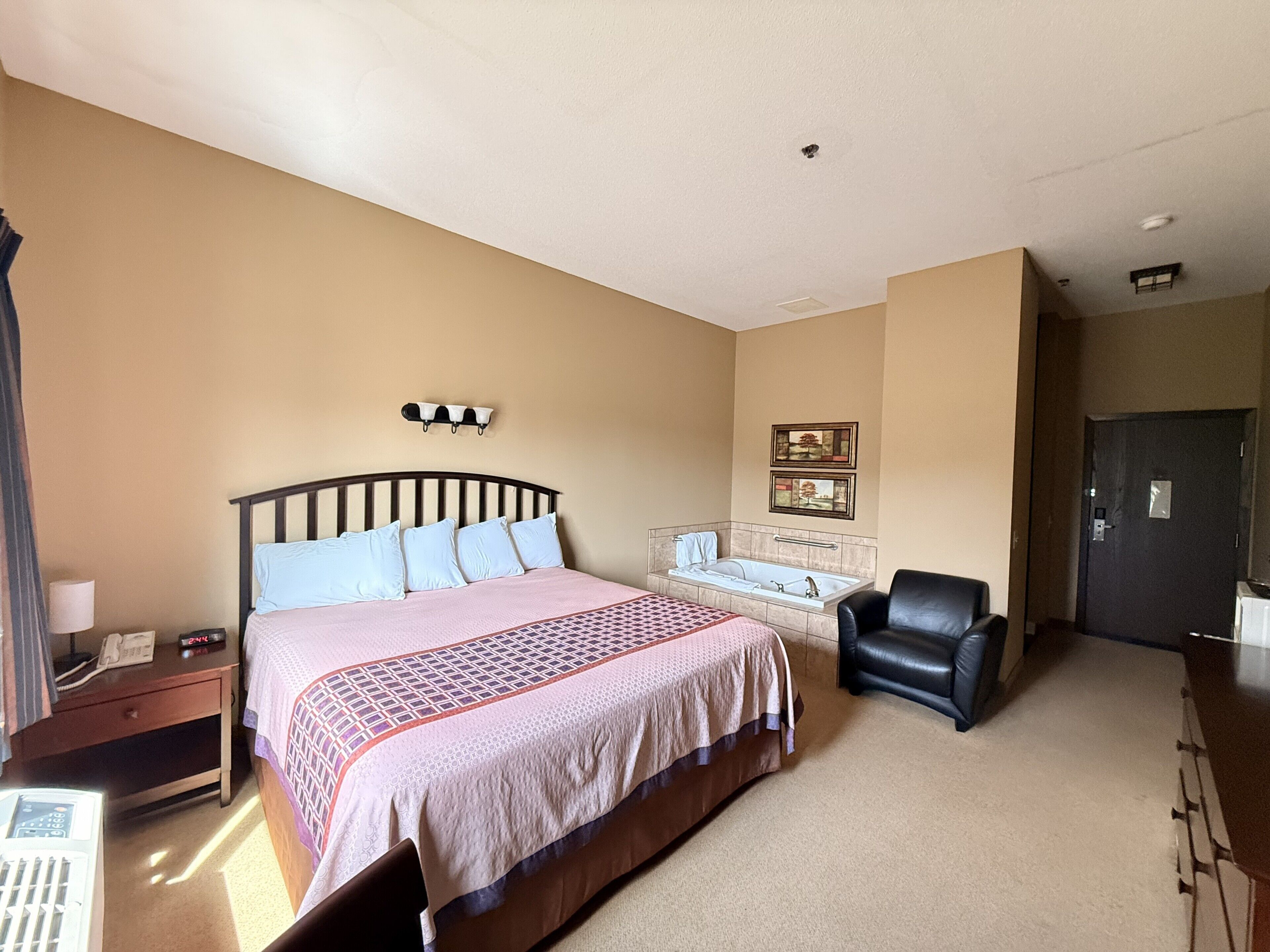 A hotel room with a bed, a desk with a telephone, a chair, a bathroom with a bathtub, and a door.
