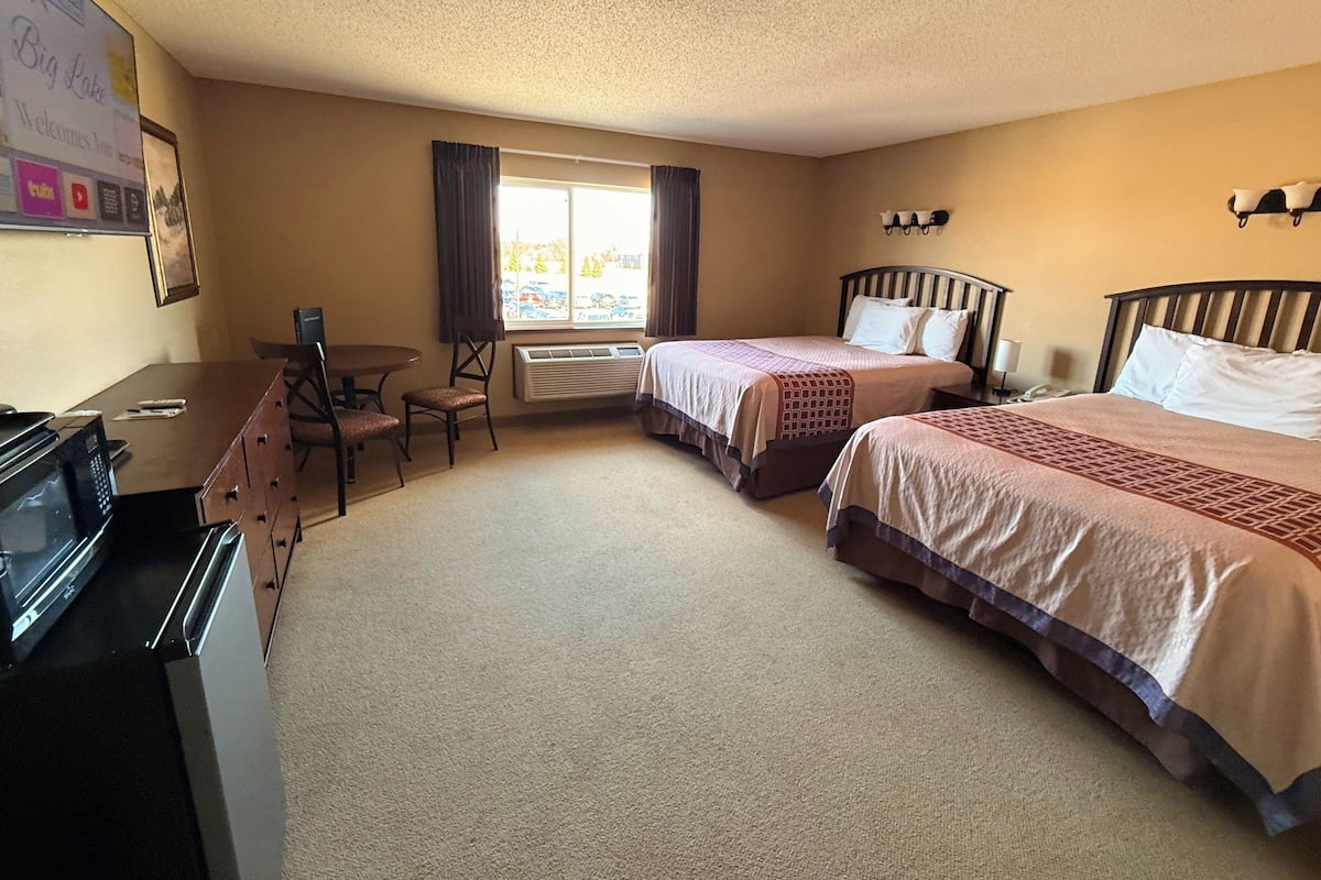 A hotel room with two beds, a desk, a chair, and a microwave.