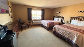 A hotel room with two beds, a desk, a chair, and a microwave.