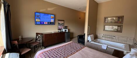 A hotel room with a bed, a desk, a TV, a bathroom, and a view of the outdoors.