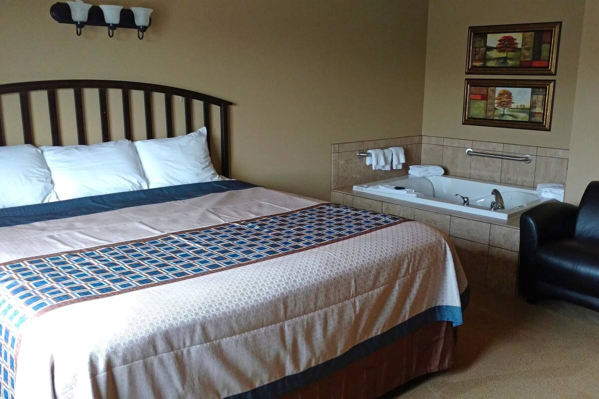 A hotel room with a bed, a chair, a bathtub, and towels on a rack.