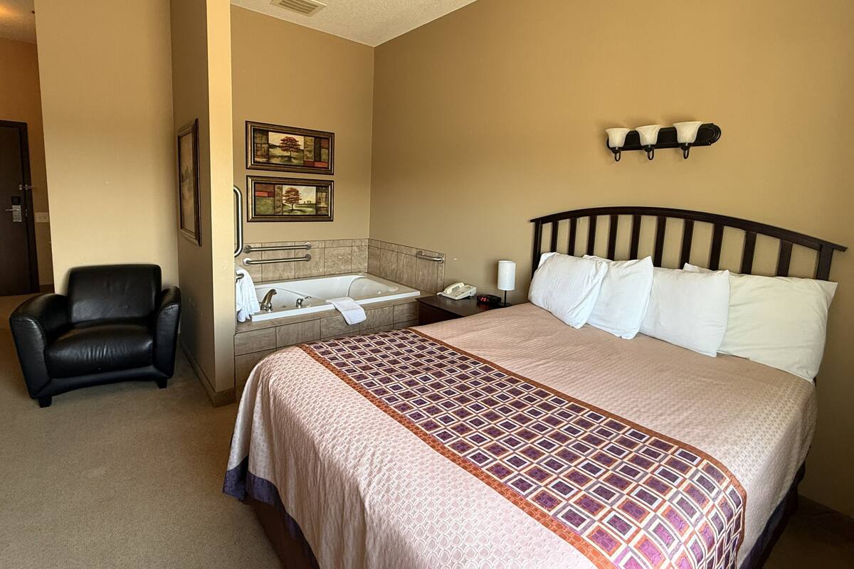 A hotel room with a bed, a chair, a bathtub, and a nightstand with a lamp.