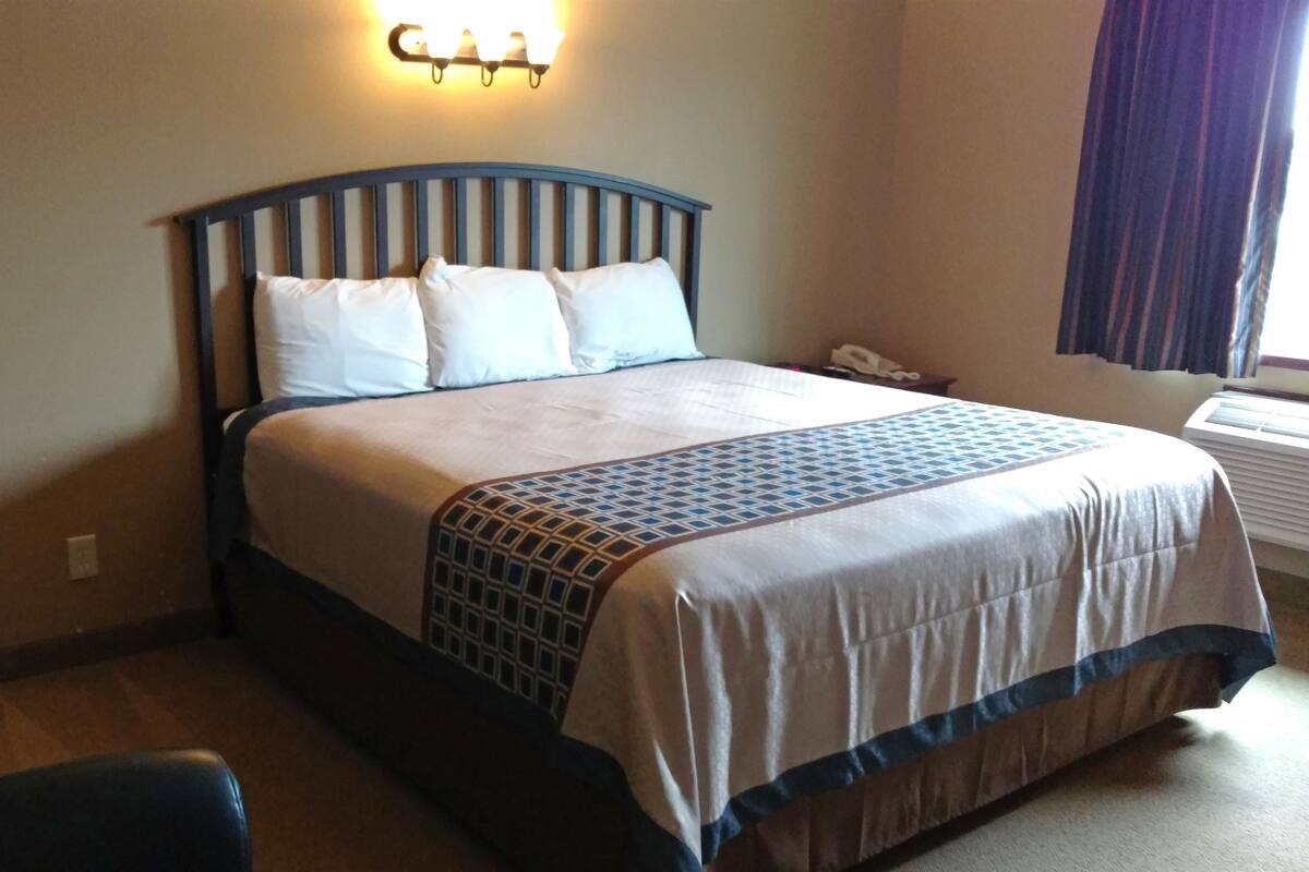 A neatly made bed with a patterned bedspread, a wall-mounted light fixture, and a window with curtains.