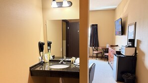Een hotelbadkamer met een wastafel, spiegel, haardroger en een klein prullenbakje.
