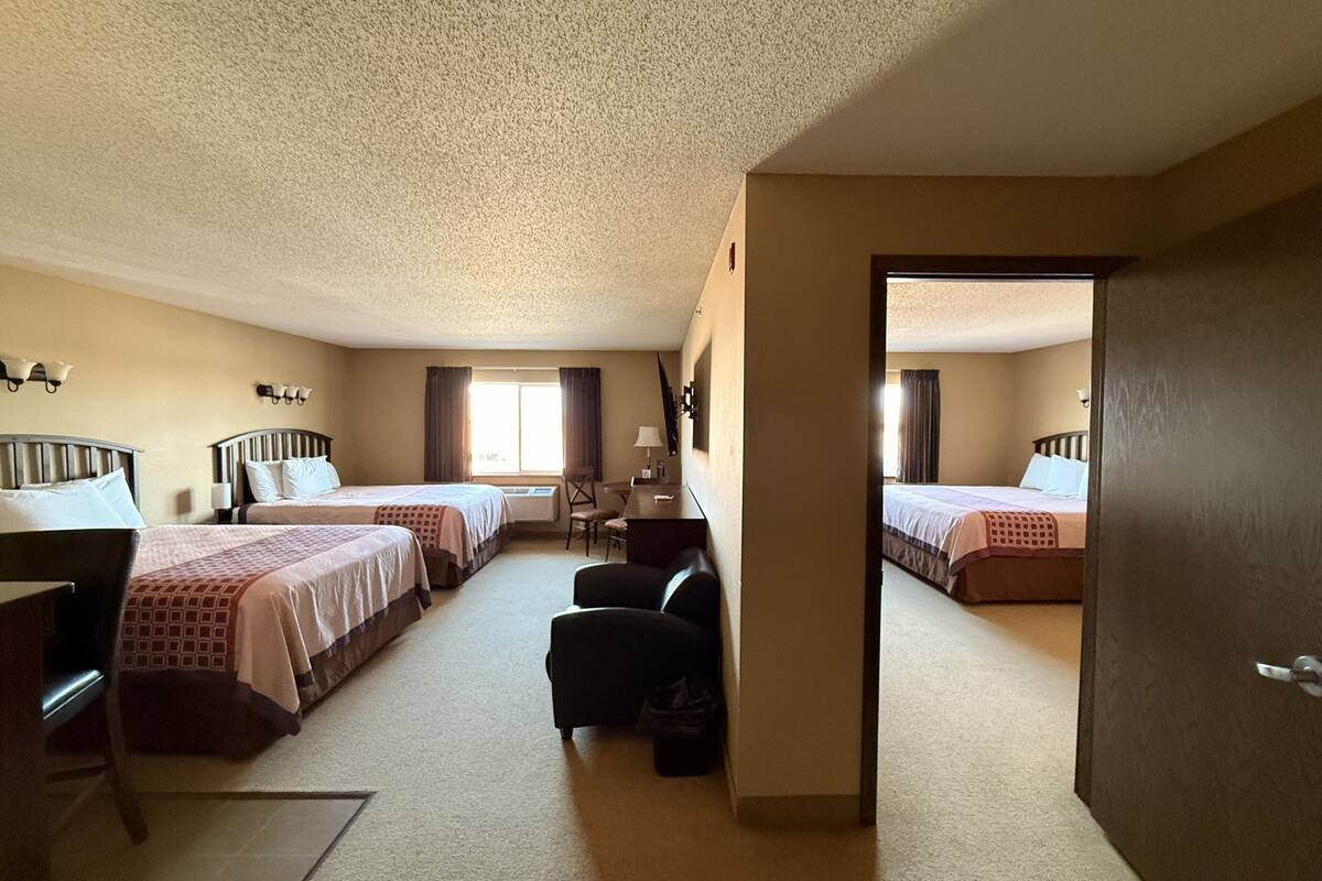 A hotel room with two beds, a desk, a chair, and a small table.
