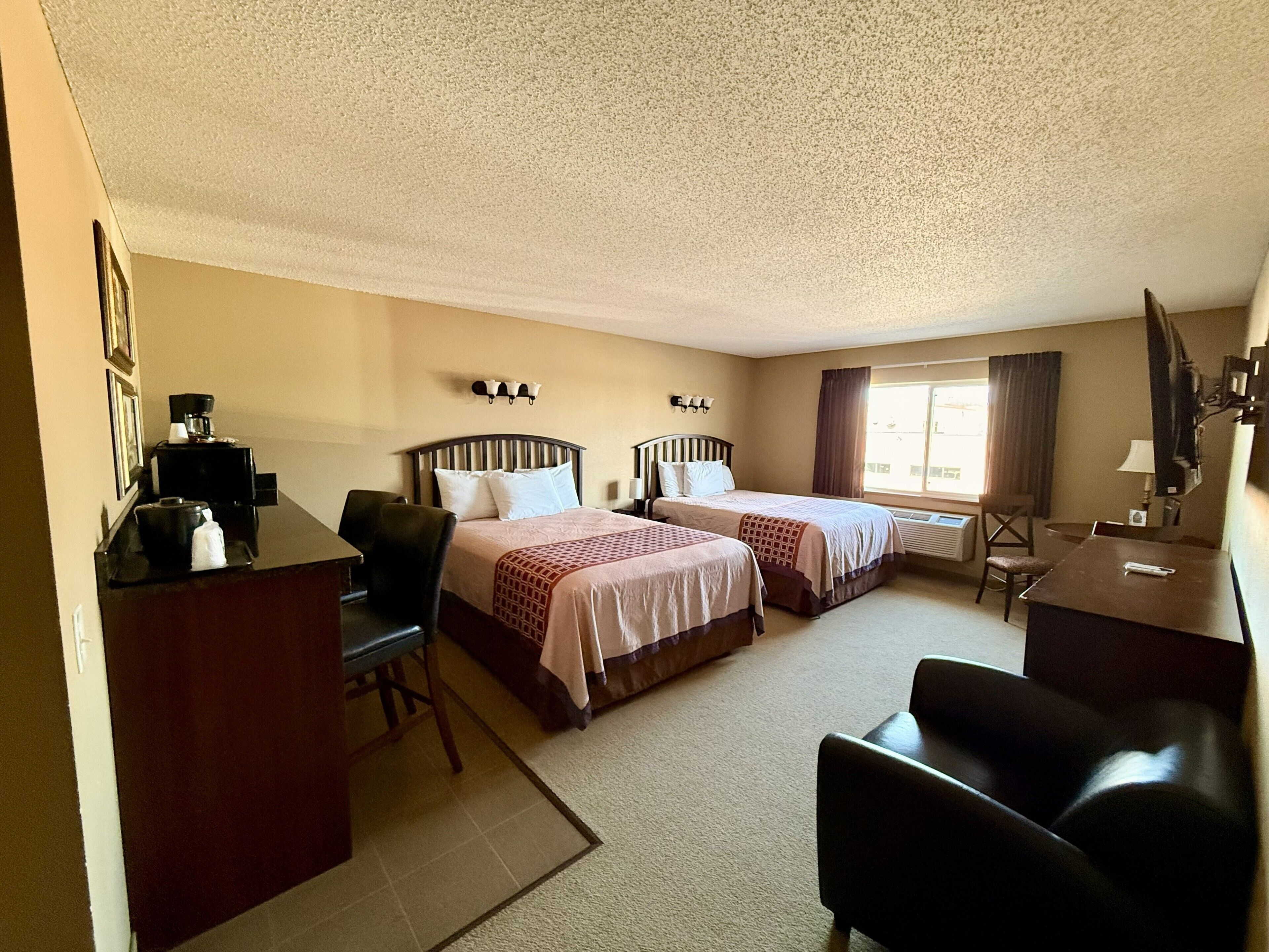 A hotel room with two beds, a desk with a coffee machine, a chair, a TV, and a window with curtains.
