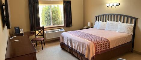 Habitación de hotel con cama, escritorio, silla y ventana con cortinas.