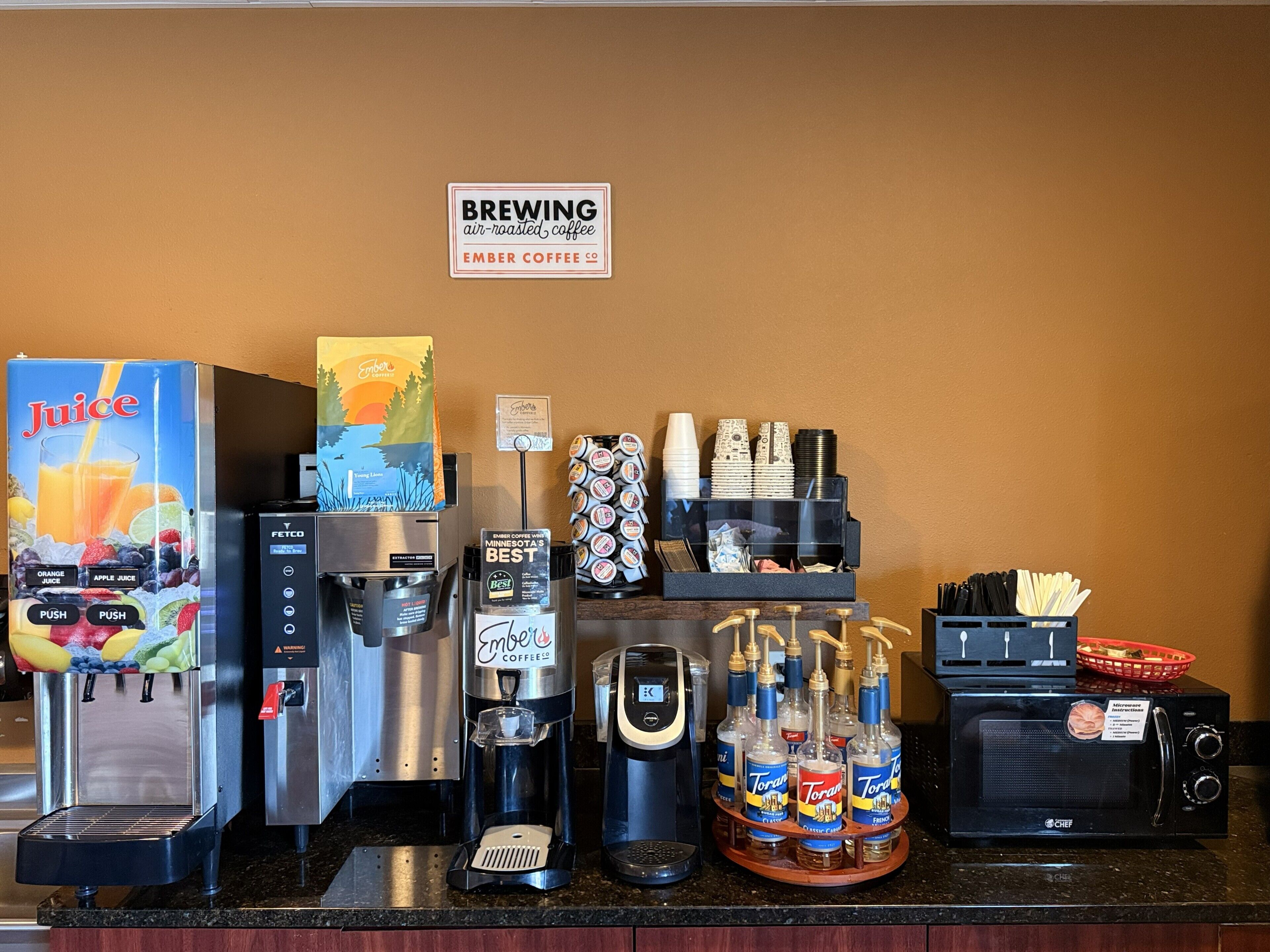 A coffee station with a juice dispenser, a coffee machine, a Torani syrup dispenser, and a microwave.