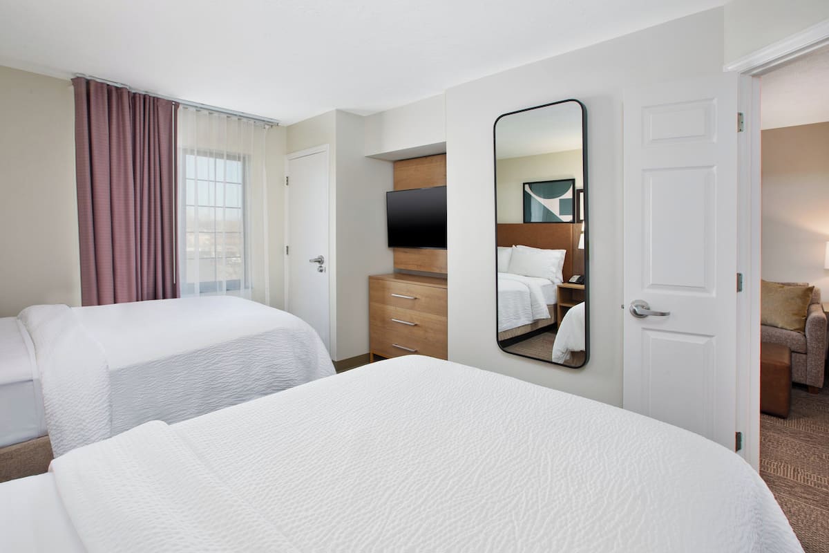 A hotel room with two beds, a wooden dresser, a flat-screen TV, and a large mirror.
