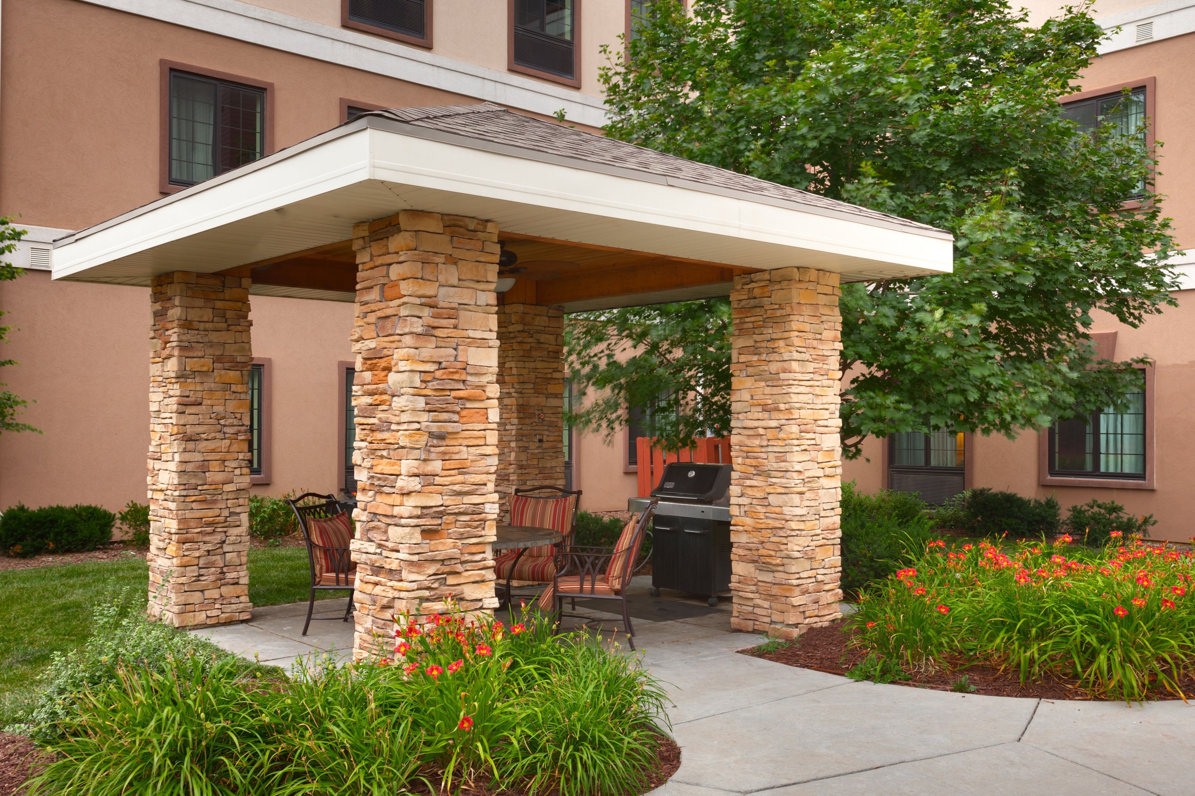 A covered patio with stone pillars, outdoor seating, and a grill.