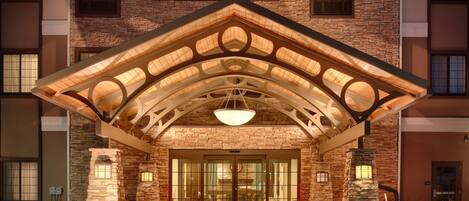 A hotel entrance with a stone facade, a covered entrance area, and a modern light fixture.
