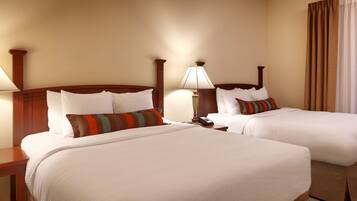 A hotel room with two beds, each with white linens and multiple pillows. There is a bedside table with a lamp and a telephone.