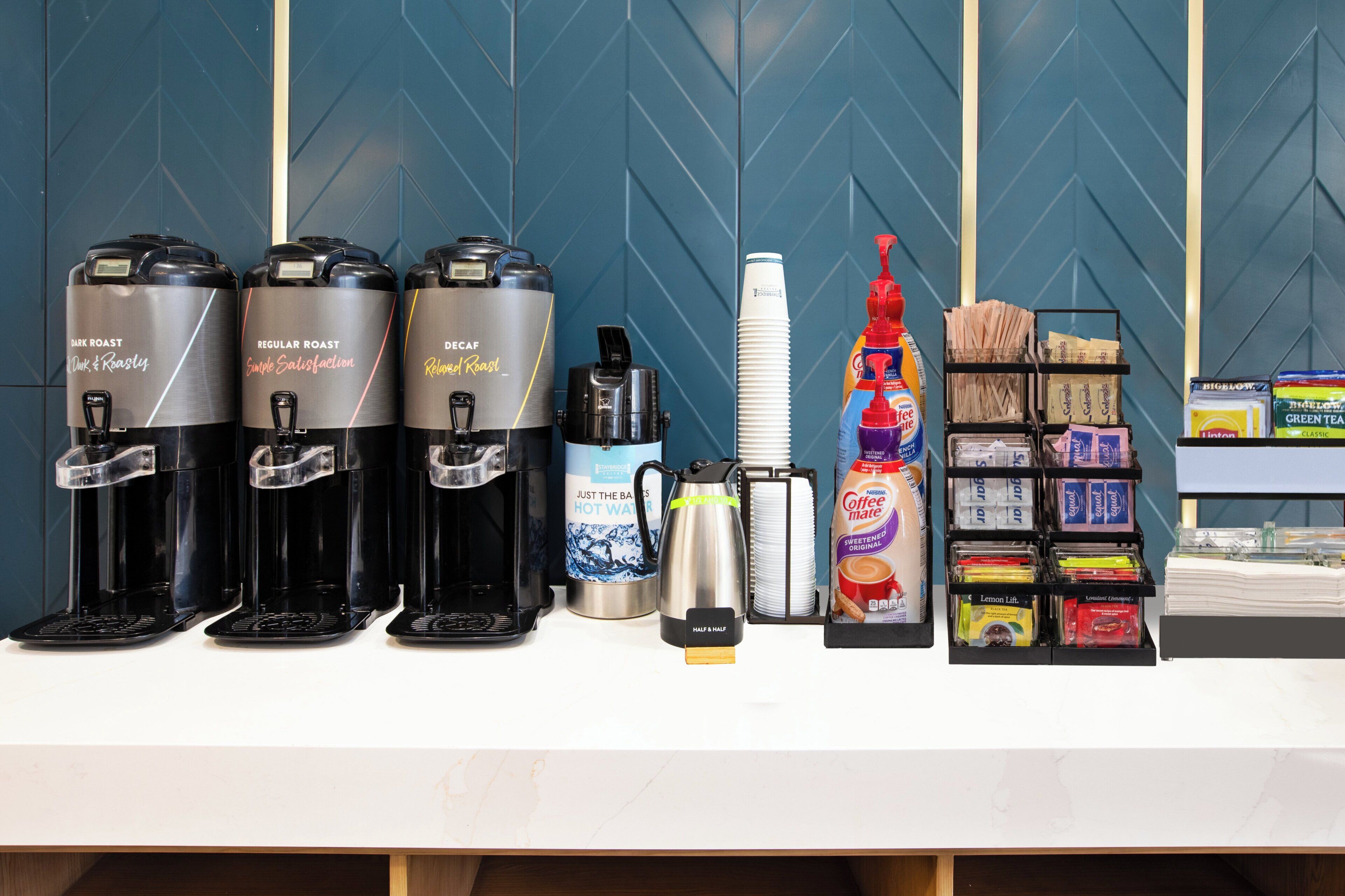 A coffee station with multiple coffee makers, a kettle, disposable cups, and a coffee machine.