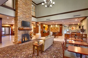 A spacious lobby with a stone fireplace, a television mounted on the wall, and a coffee bar area. - Staybridge Suites Omaha 80th And Dodge by IHG (Omaha)