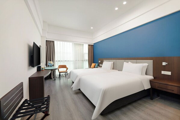 Ein Hotelzimmer mit zwei Betten, einem Schreibtisch, einem Sessel, einem Fernseher und einem Fenster mit Vorhängen.