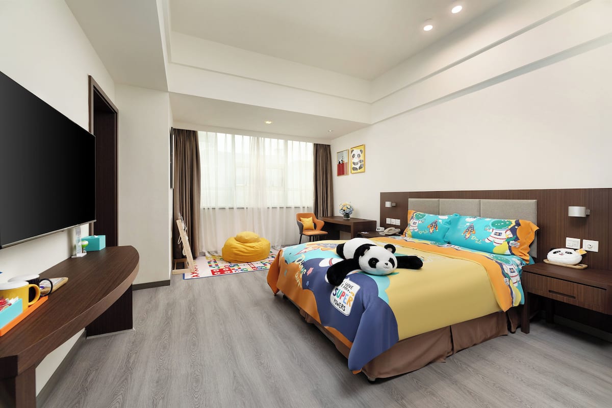 A hotel room with a bed, bedside table, lamp, and a TV.