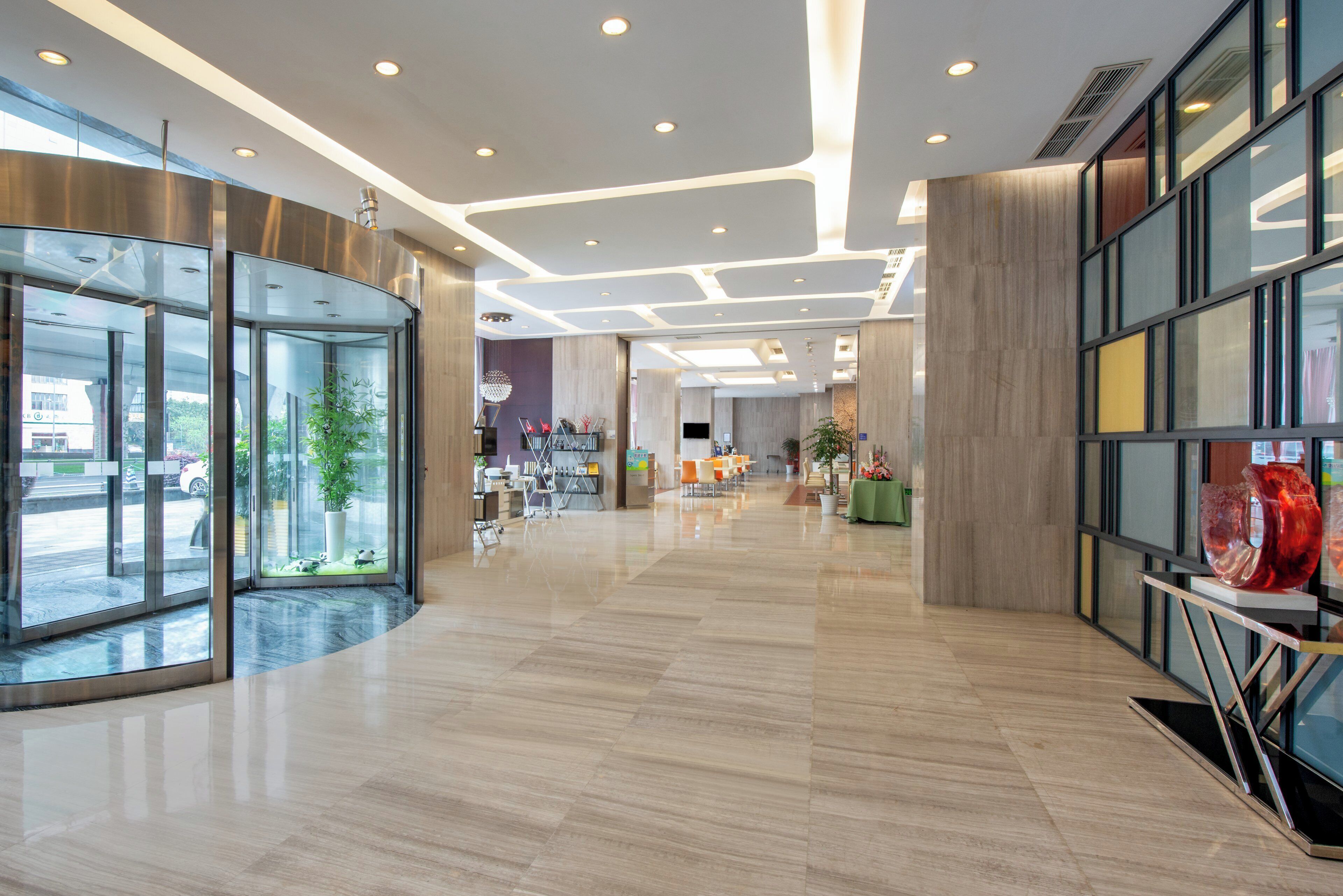 A modern hotel lobby with glass doors, a reception desk, and a seating area.