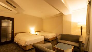 Habitación de hotel con dos camas, un sofá, una mesita y una lámpara.