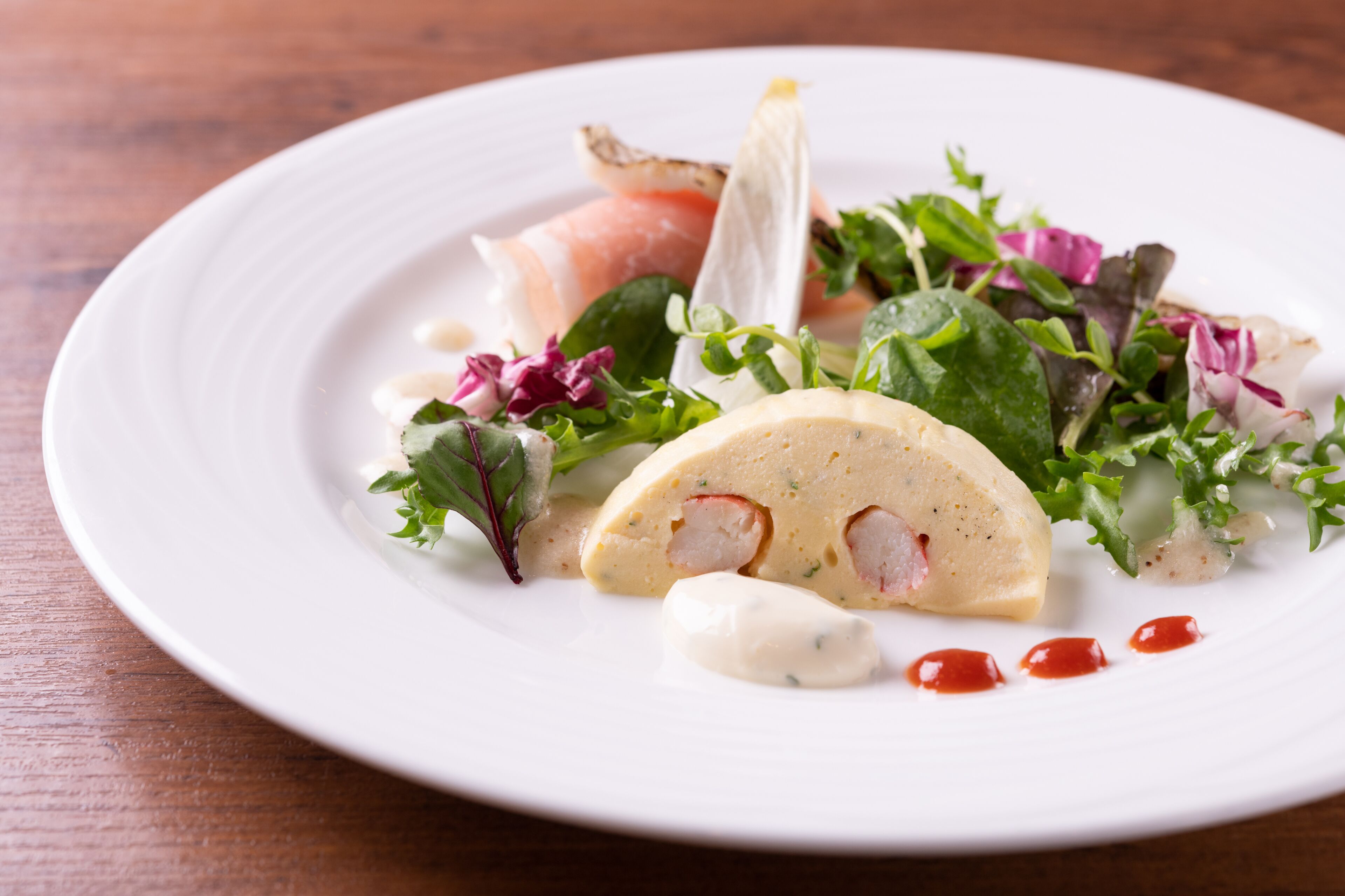 A white plate with a salad, including greens and a creamy item, on a wooden table.