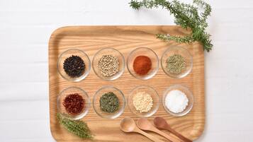 A wooden tray with glass bowls containing various spices and herbs, accompanied by wooden spoons and fresh thyme.