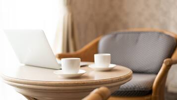 A wicker chair with a laptop and two white cups on a round table.