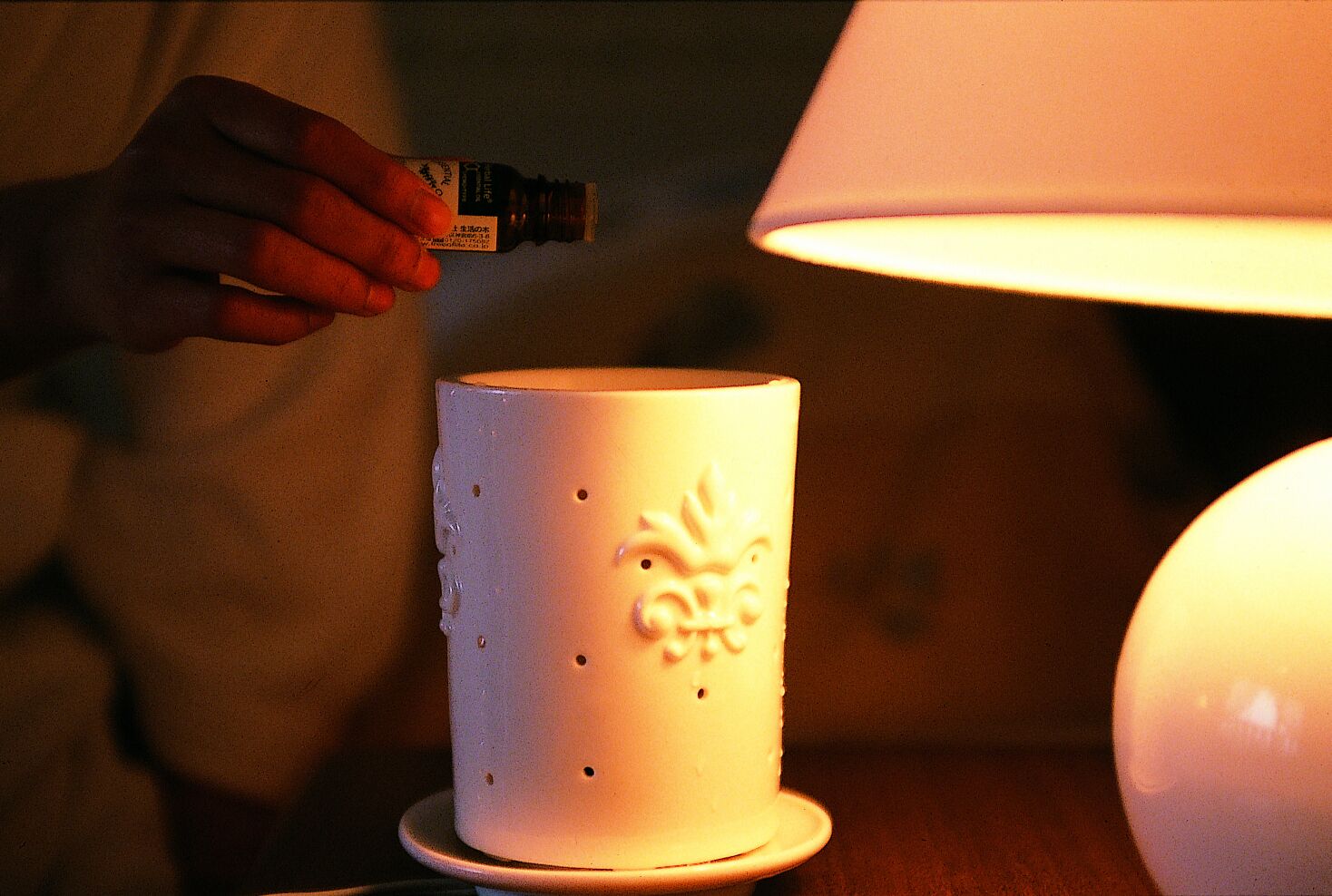 Una mano sosteniendo una botella cerca de un candelabro blanco con diseños en relieve.