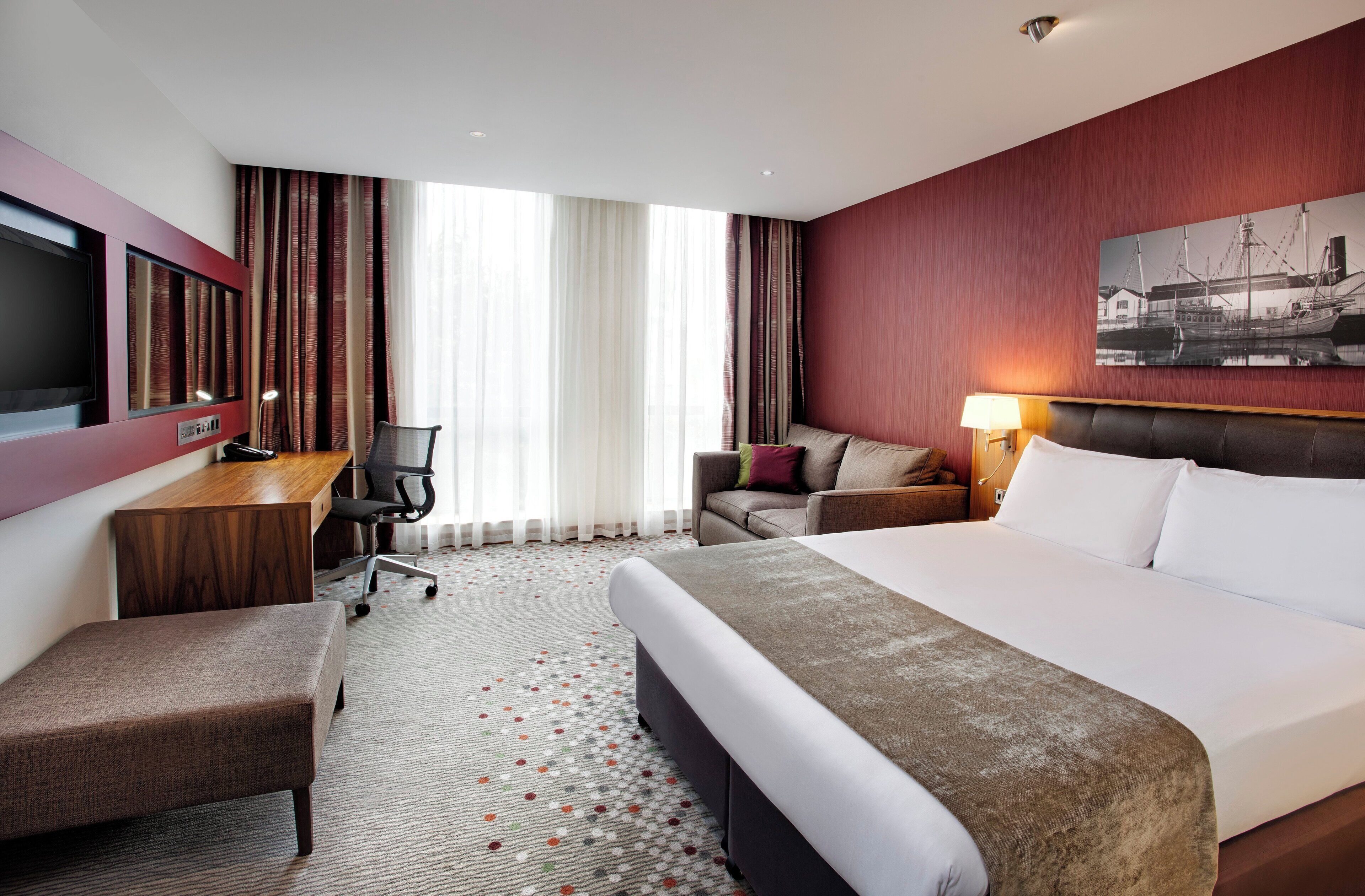 A hotel room with a bed, a desk, a chair, a sofa, and a TV.