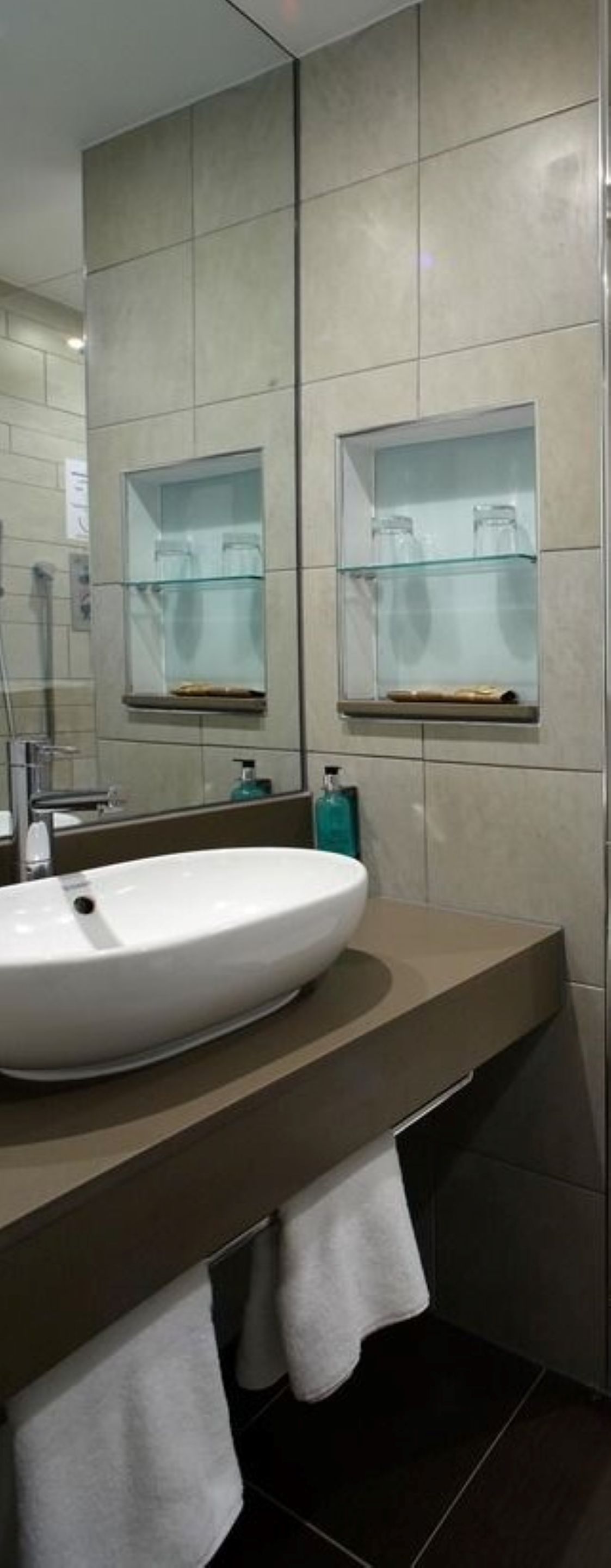 Une salle de bain moderne avec un grand miroir, un lavabo blanc et deux armoires à pharmacie à façade en verre.