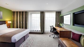 A hotel room with a bed, desk, chair, television, and curtains.