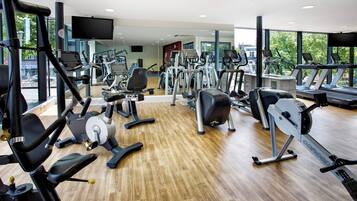 A gym with various exercise equipment, large windows, and a wooden floor.