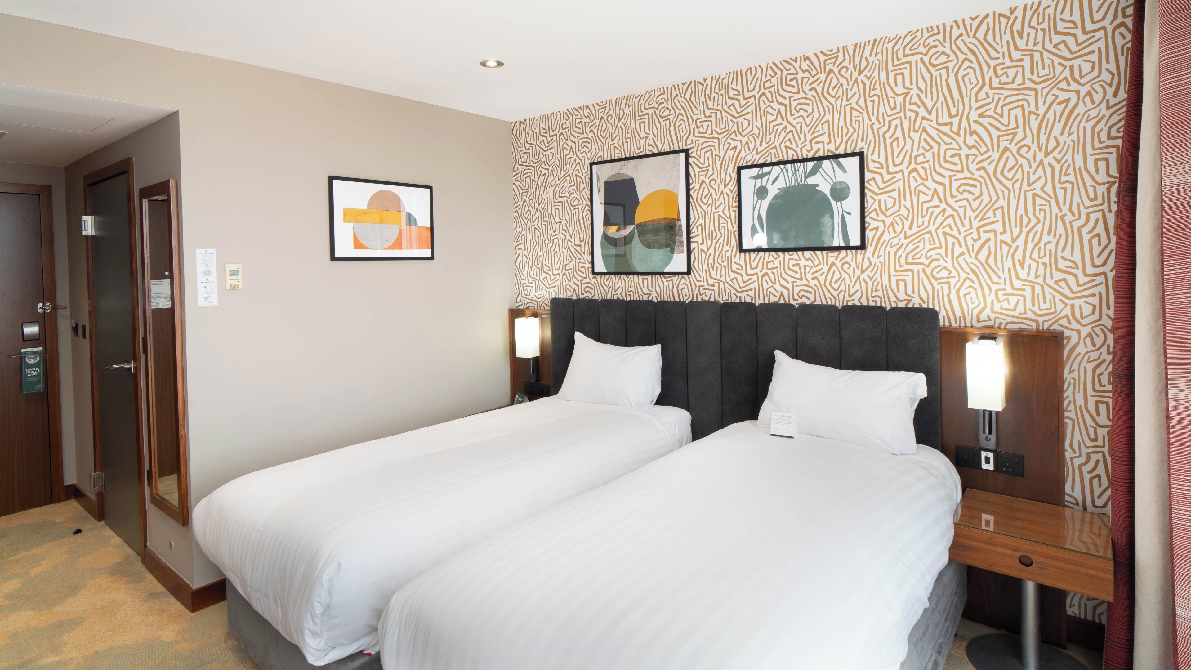 A hotel room with two beds, a patterned wall, and two framed artworks.
