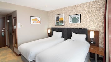 A hotel room with two beds, a patterned wall, and two framed artworks.